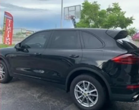 A black Porsche Cayenne with dark tinted windows beside a red “Tinting” flag