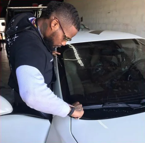 An installer in glasses working film at the edge of a white car’s window