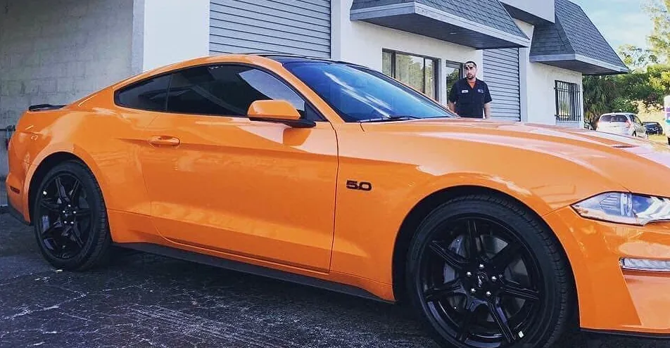 An orange Ford Mustang GT with freshly tinted windows parked outside the tint shop